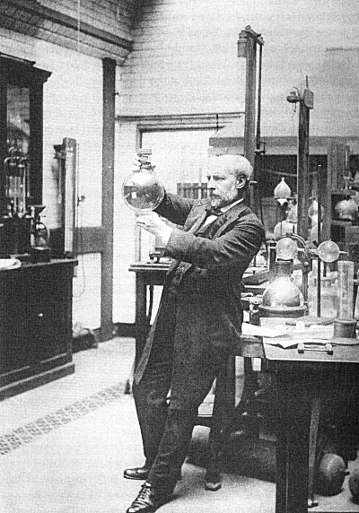 James Dewar in the Royal Institution in London, around 1900.

Dewar’s expression in such photographs is usually one of deep concentration or mild seriousness, reflecting his dedication to scientific inquiry. 

He is often dressed in formal attire, wearing a dark suit or frock coat typical of the period, which adds to the impression of professionalism and authority. 

Dewar's hair in these photographs is generally short and well-kept, with a full mustache, which was typical of men in the late Victorian and early Edwardian periods. 

Dewar is standing with a hand holding a dewar. 