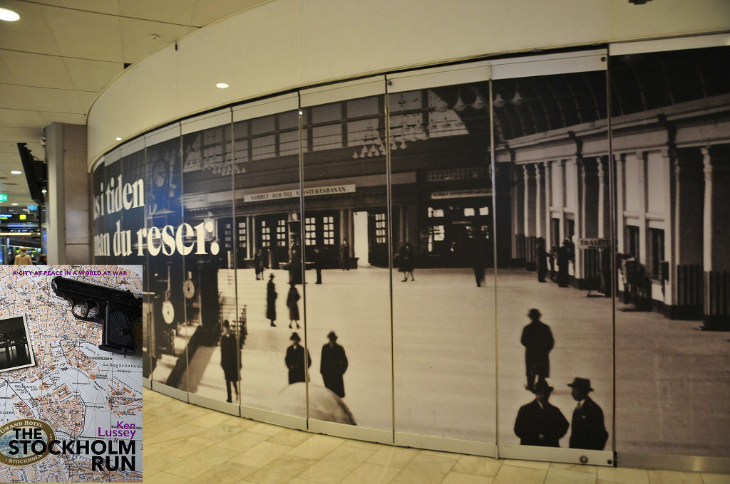 Stockholm Central Station. The image shows a curving segmented wall that comes in from the right of the frame and extends away from us near the left side. The wall carries a very large black and white photograph of the interior of the station in 1943, with ticket offices on the right and doors to the outside in the background and people, mainly wearing hats. The front cover of 'The Stockholm Run' is shown in the bottom left corner.