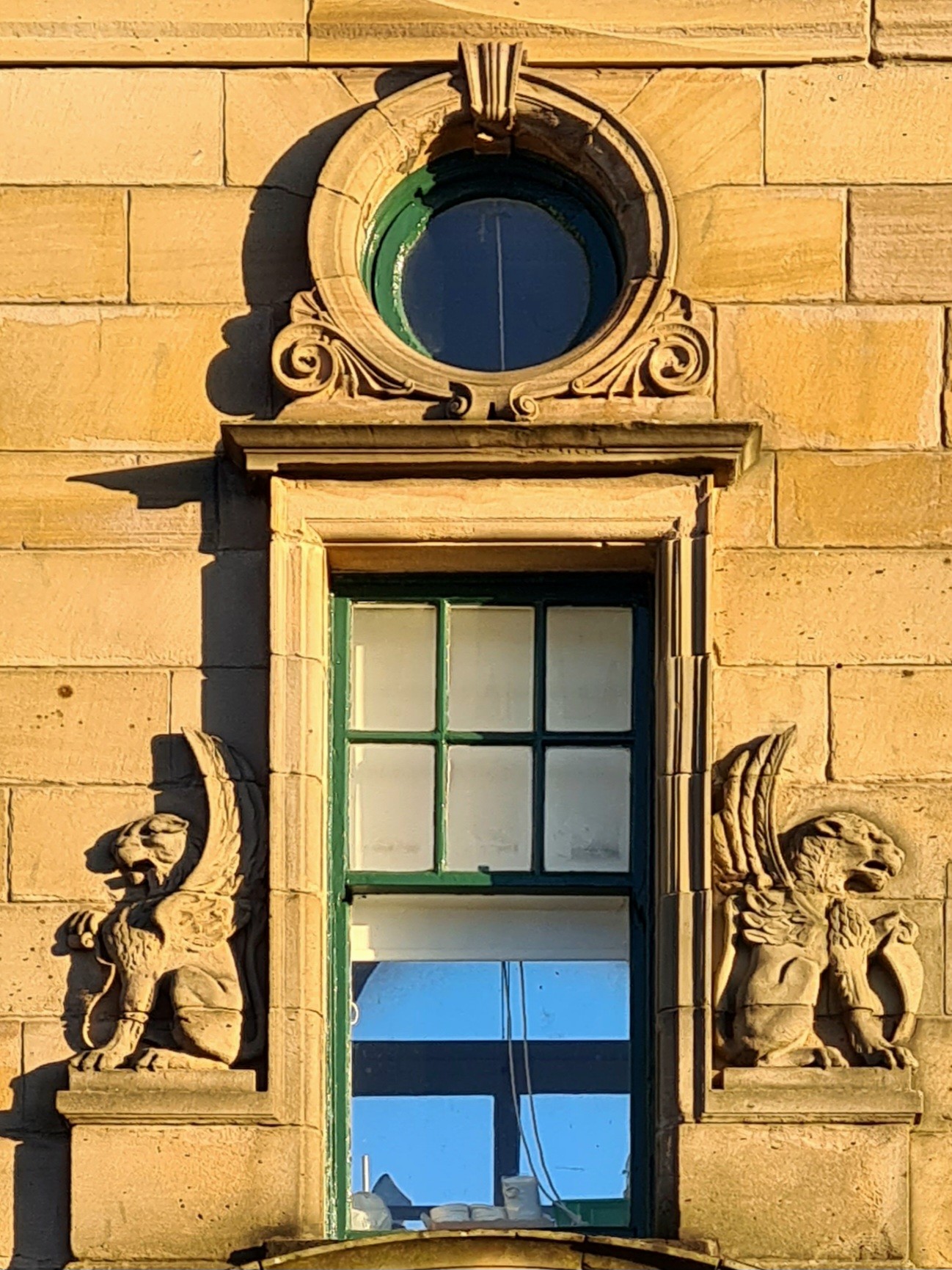 A rectangular window with winged lions on either side and topped by a smaller circular window.