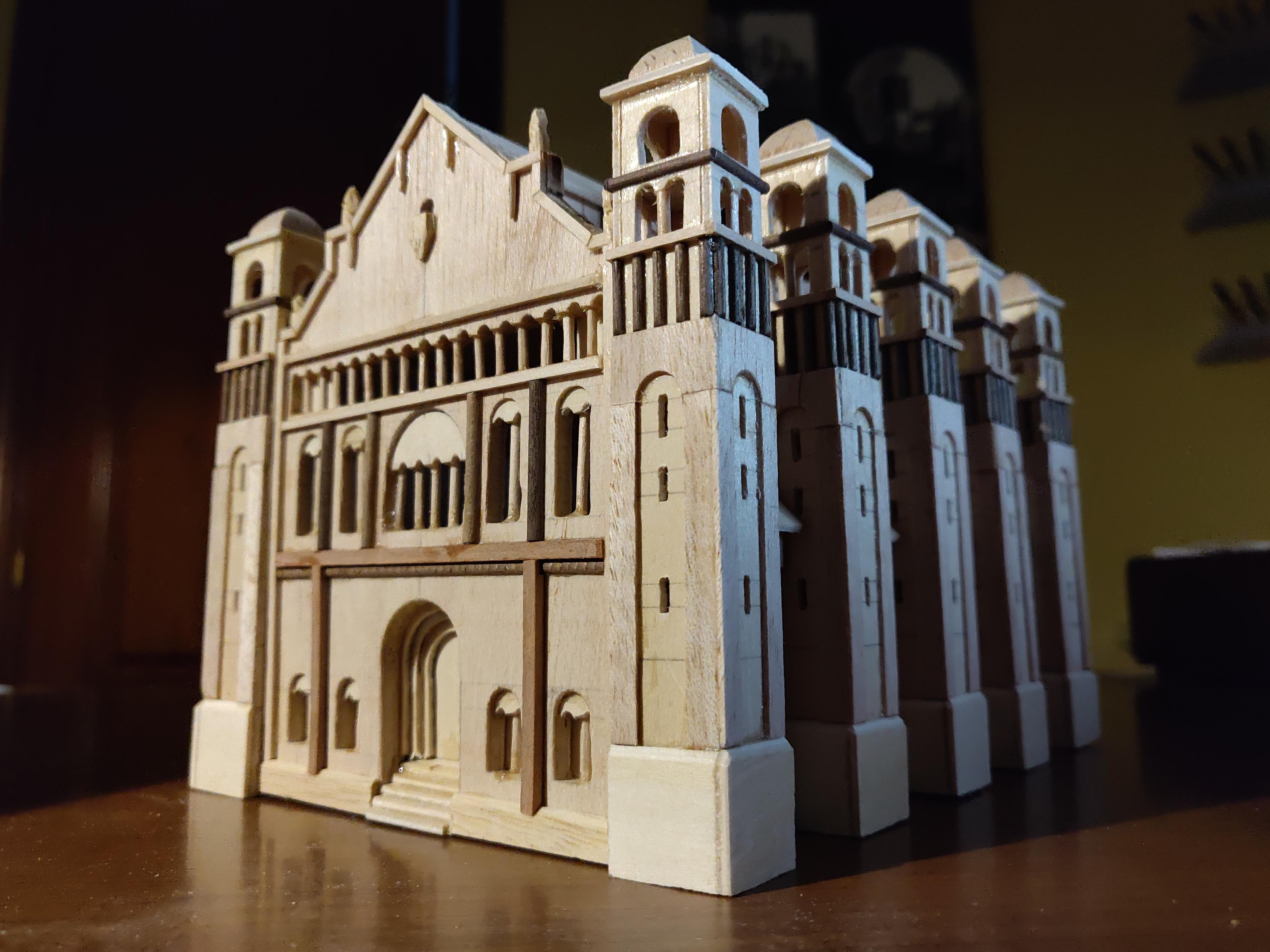 A very detailed wooden model of a building similar to a church or a castle. It has a triangular roof, five towers on each side, and an arched door and windows at the front.