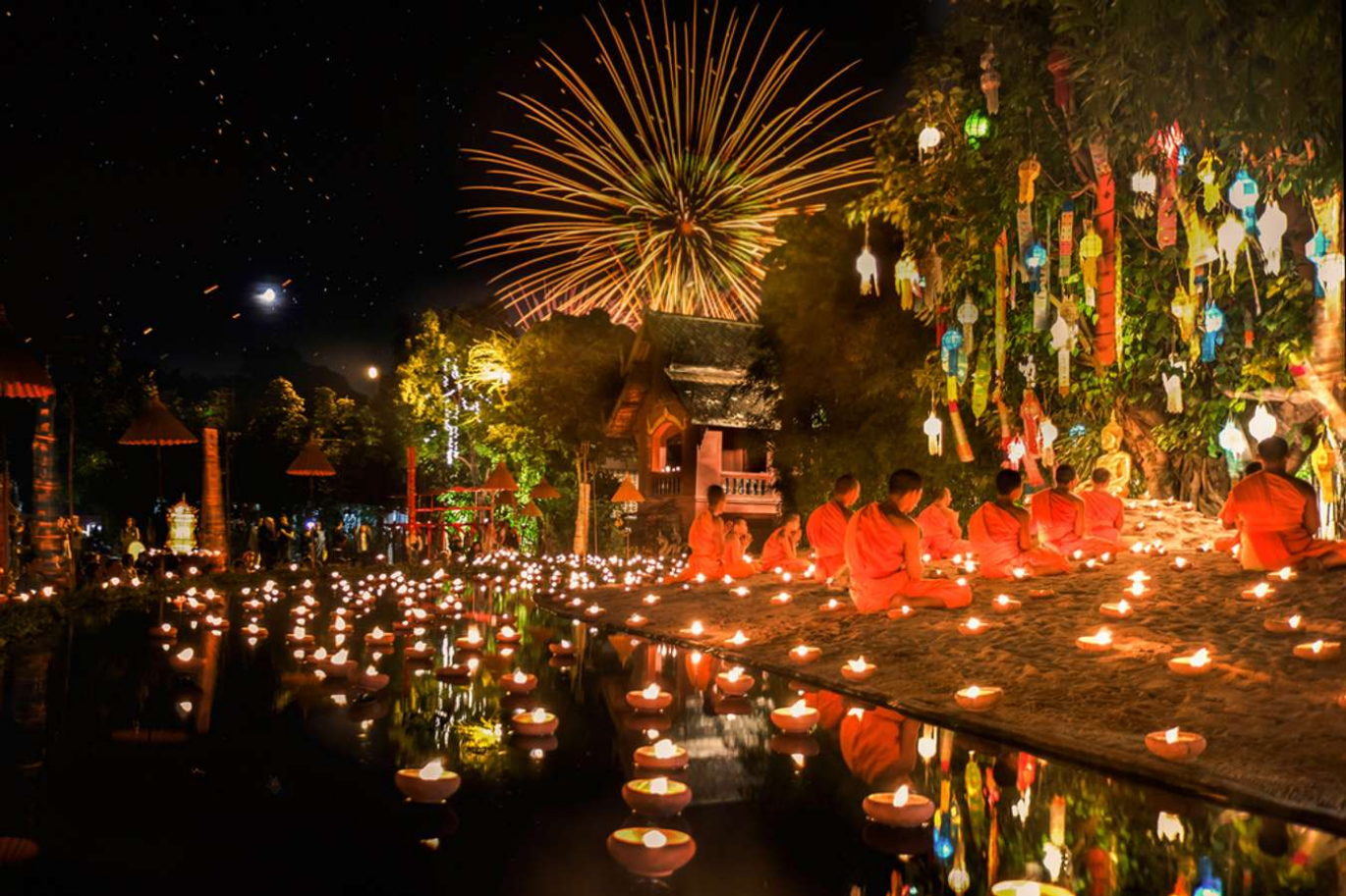 a photo of monks praying in front of a tree, there is a river behind them with small boats with candles on them, fireworks in the background, all the lights glowing in the night  