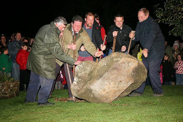 A group of men gather round a huge boulder, trying to turn it over