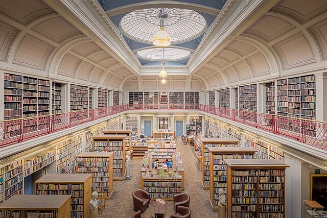 Spectacular interior of Newcastle's Lit and Phil Library, with vaulted ceiling, second floor galleries with red ironwork railings, and large circular skylights.