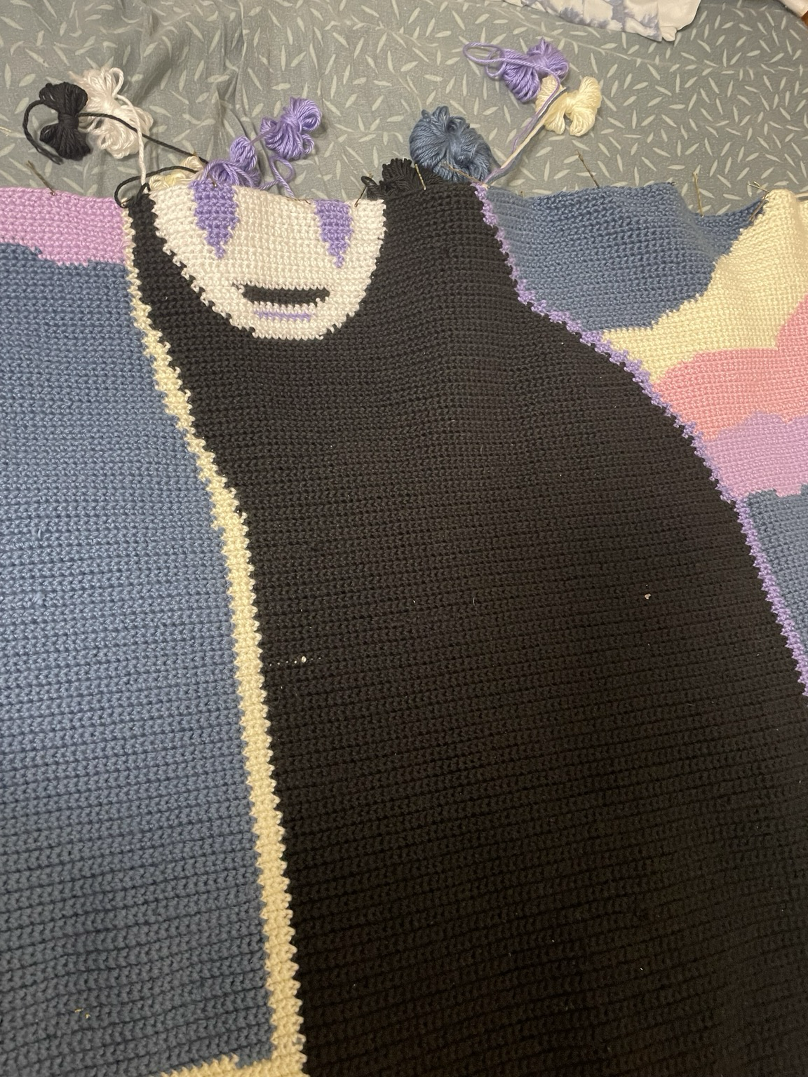 A close up photo of a crochet blanket depicting the partially complete face of NoFace from Spirited Away. 