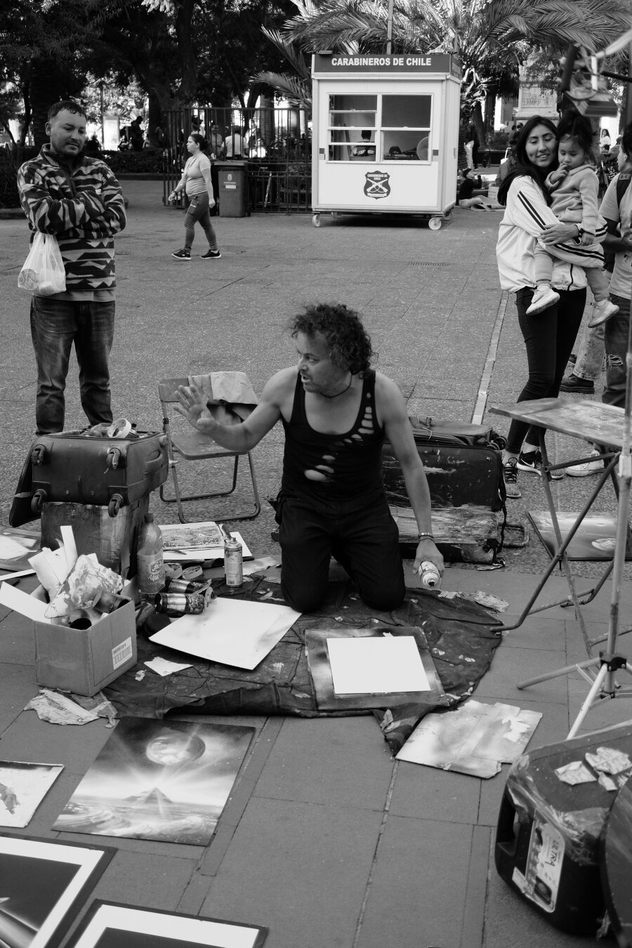 Man on his knees in front of a canvas on the ground with art and art materials scattered around him