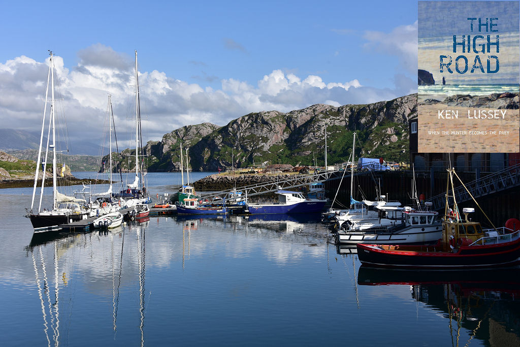The image shows a view of a harbour in bright sunlight. The water is calm and extends from the bottom of the frame to a dozen or so small boats moored at pontoons across the centre of the frame, with a quayside and buildings on the right. In the background a rocky shoreline rises from the water and there are hills in the distance in the left centre of the frame. The front cover of ‘The High Road’ is shown in the top right corner.