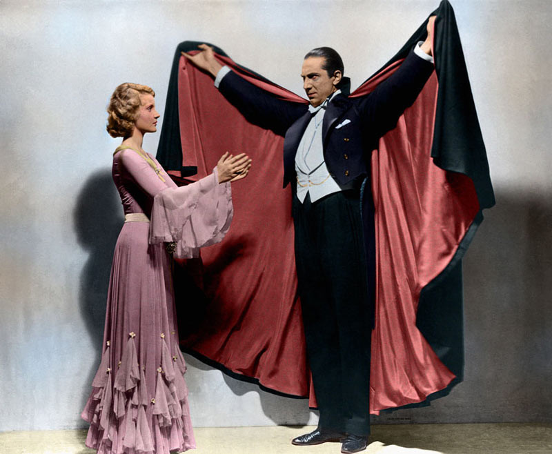 Bela Lugosi in vampire costume opening his cape in front of a blond woman in a purple dress.