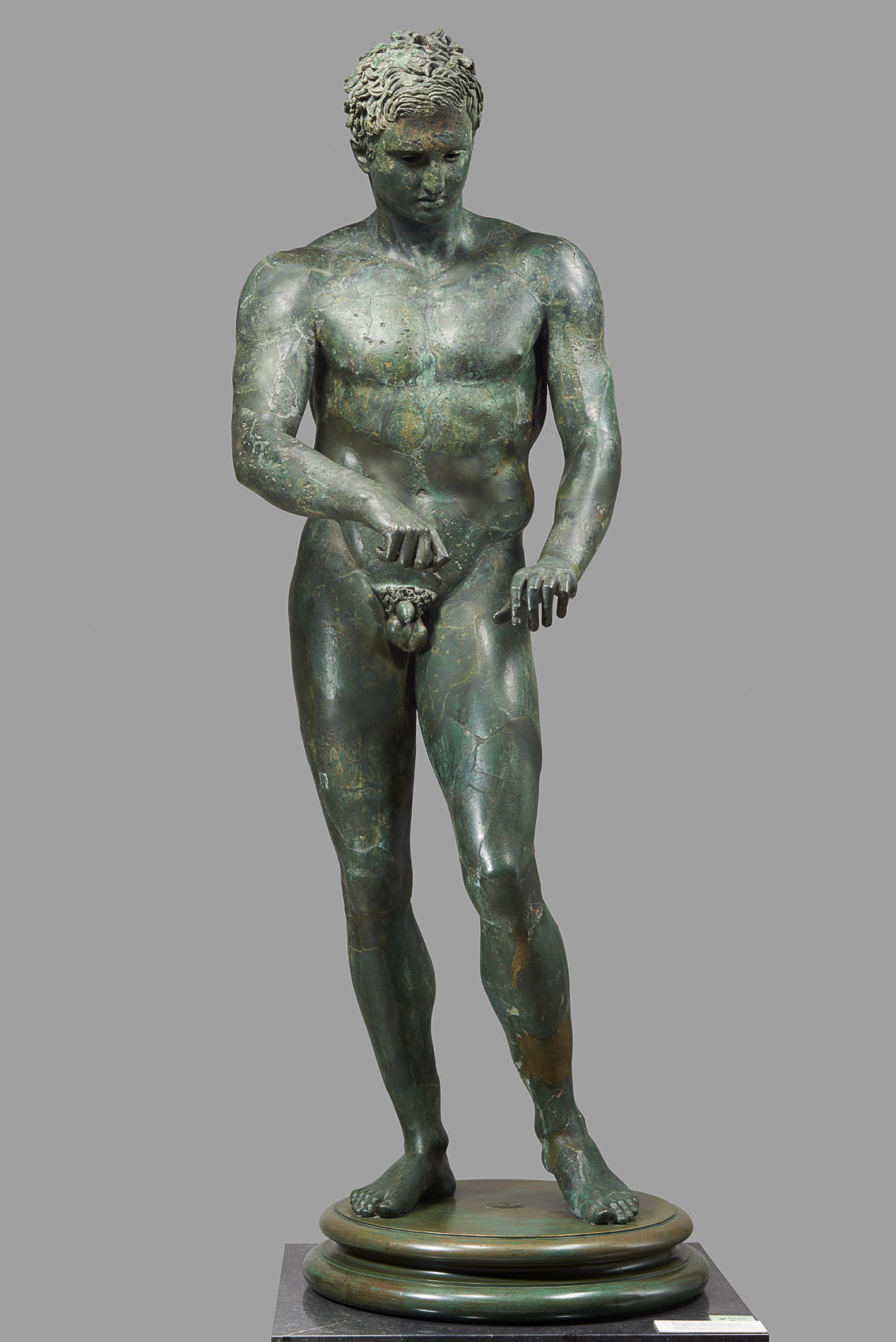 Description from the museum: “It depicts an athlete who, after completing his workout in the gymnasium’s palaestra, is shown scraping off sweat, sand and the oil he had slathered himself with with a στλεγγίς (strigilis). We see him running his left thumb over the (now lost) scraper to clean it. Both the apparently spontaneous “snapshot” of someone lost in thought, and stylistic details point to a 4th-century BC model. Recently it has been suggested that the statue is a copy of Lysippos’ celebrated “Apoxymenos” (the scraper).”