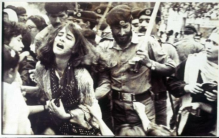 A policeman appears to have a woman in an armlock as they move through a crowd.