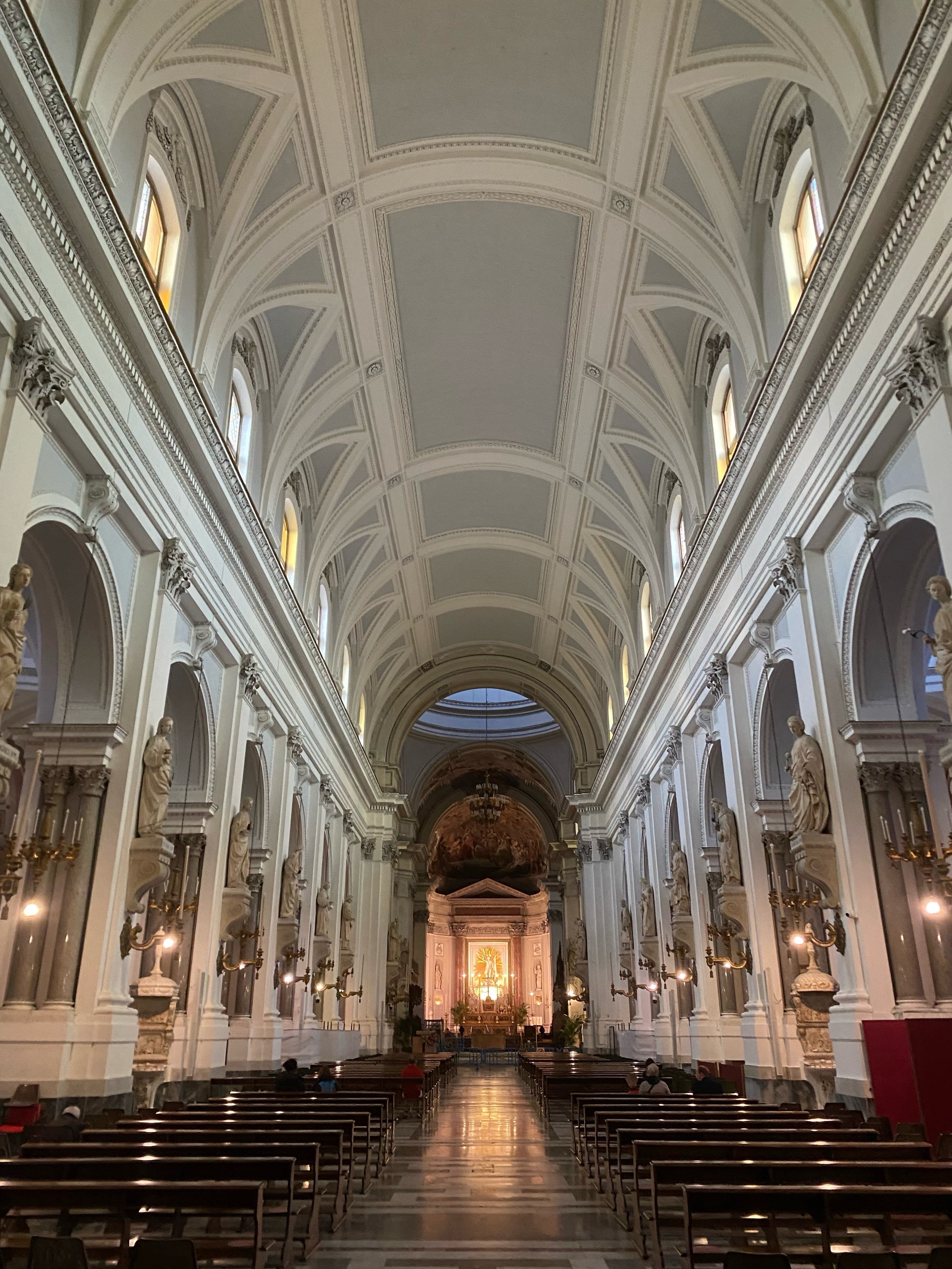 Interior of a cathedral with vaulted ceilings & rows of statues along the walls leading to an altar at the end of the aisle.