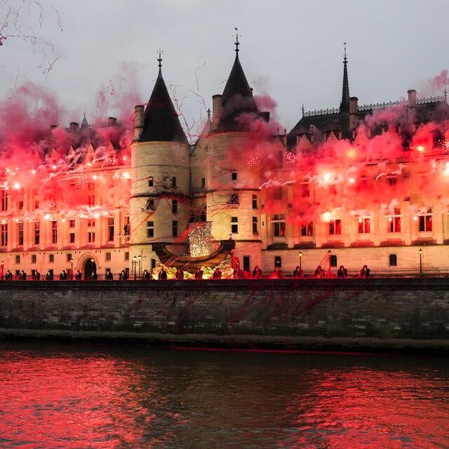 Conciergerie in Paris lit by hundreds of red explosive pyrotechnics with a viking boat floating in front of it.