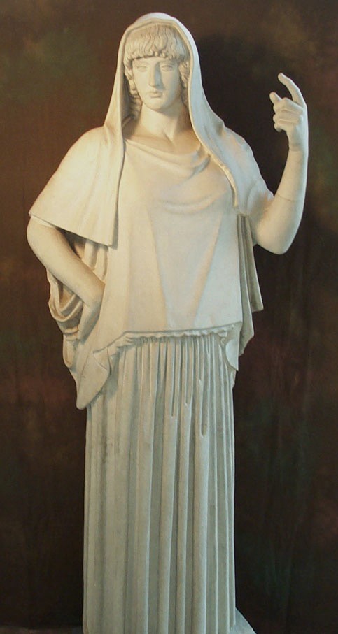 The statue represents Hestia, the Greek goddess of the hearth, home, and domestic life. She is often depicted as a modest, serene figure, embodying stability and warmth. In this sculpture, Hestia is shown standing in a calm and composed posture, draped in a long, pleated robe that covers her entire body, symbolizing her modesty and dedication to domesticity. The veil covering her head is a common feature in depictions of her, emphasizing her purity and association with the sacred hearth. Her raised hand, with the index finger extended, may symbolize the sacred flame she guards or a gesture of blessing or protection over the household.

This peaceful and nurturing depiction reflects Hestia's essential role in maintaining harmony in both the home and the wider community in ancient Greek religion.