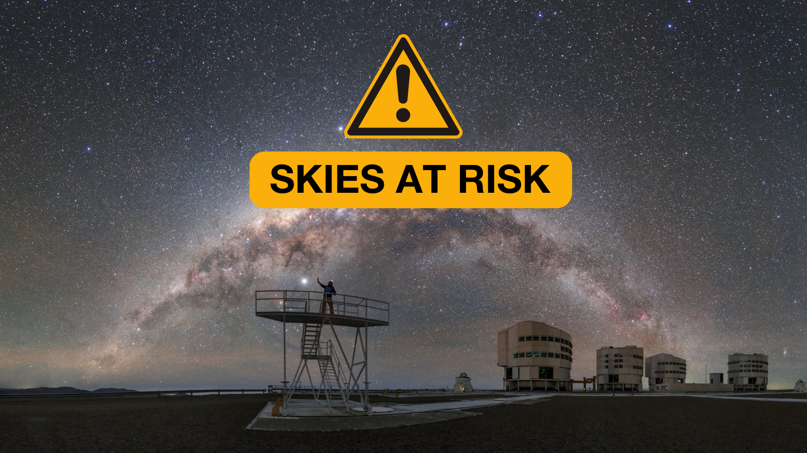 A view of the Milky Way arching across the night sky above the Atacama Desert in Chile. The foreground features the buildings of ESO’s Very Large Telescope (VLT), with a person standing on a raised platform. A sign saying "skies at risk" is overlaid on the image.