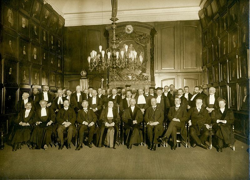 photo of the academic staff of Utrecht university in a room where the walls are all paintings of men. Johanna Westerdijk is sat in the middle of the front row. Everyone is white.