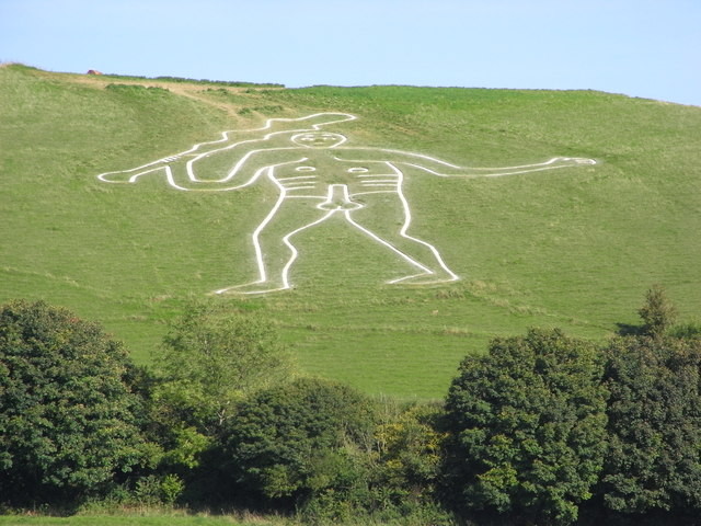 Figure of a naked giant carved into a steep, green hillside. The giant is outlined in white due to the chalk beneath the turf. The giant has a large erect penis and is waving a club over his head.