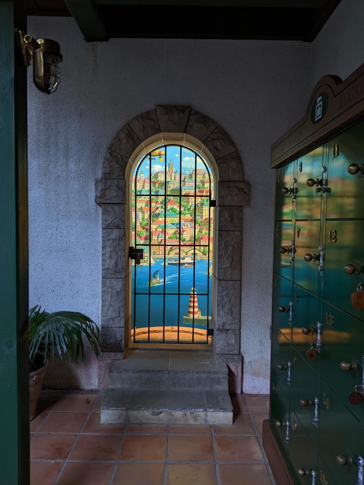 A painted area of blue sea and buildings in a small arched alcove next to coin lockers