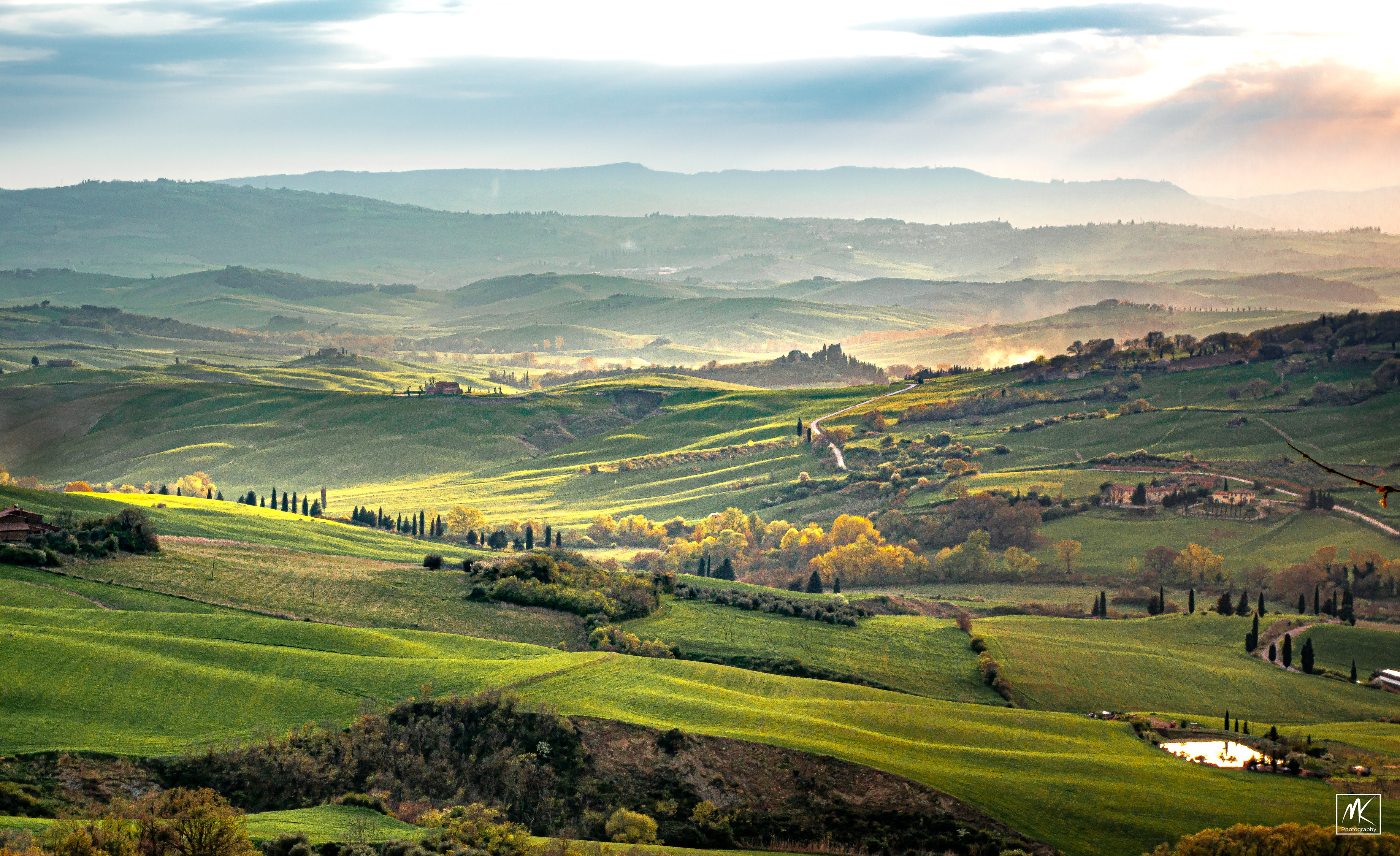 Color photo of a green Tuscan landscape near sunset with the light washing over the hills and valleys. 