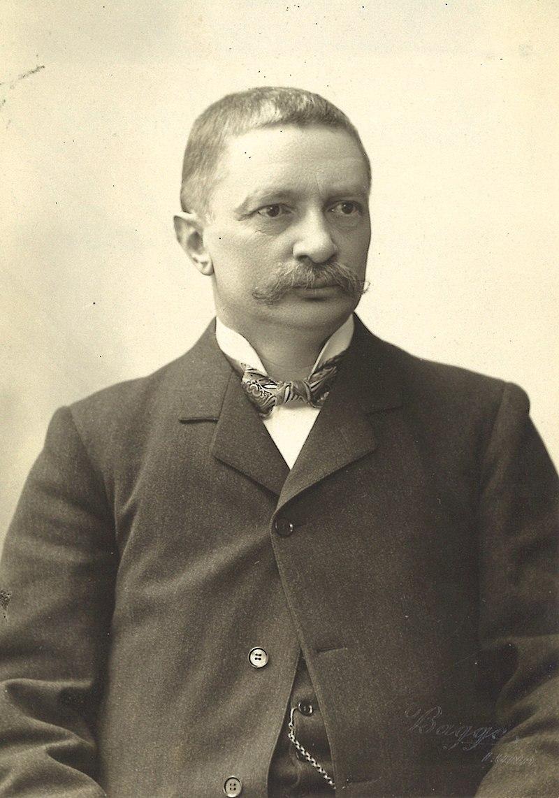 Johannes Rydberg (1854-1919), Swedish physicist and professor at Lund University.

By Per Bagge (1866-1936) - Original photograph in the collections of sv:Akademiska Föreningens Arkiv & Studentmuseum (The Archives and Museum of the Academic Society) in Lund, Sweden.

Johannes Rydberg is depicted in formal attire, consistent with the conventions of late 19th to early 20th-century portraiture. His appearance conveys dignity and intellectual depth.

Rydberg has a calm and contemplative expression, reflecting his scholarly pursuits and serious demeanor. His posture is upright, emphasizing his role as a respected academic.

The photograph likely features a neutral or slightly darkened background, a typical style in academic portraiture, which draws attention to the subject.

The lighting is soft, highlighting his facial features and beard, which were characteristic of his era. The details of his clothing, such as a suit or academic robe, add to the formal tone of the image.