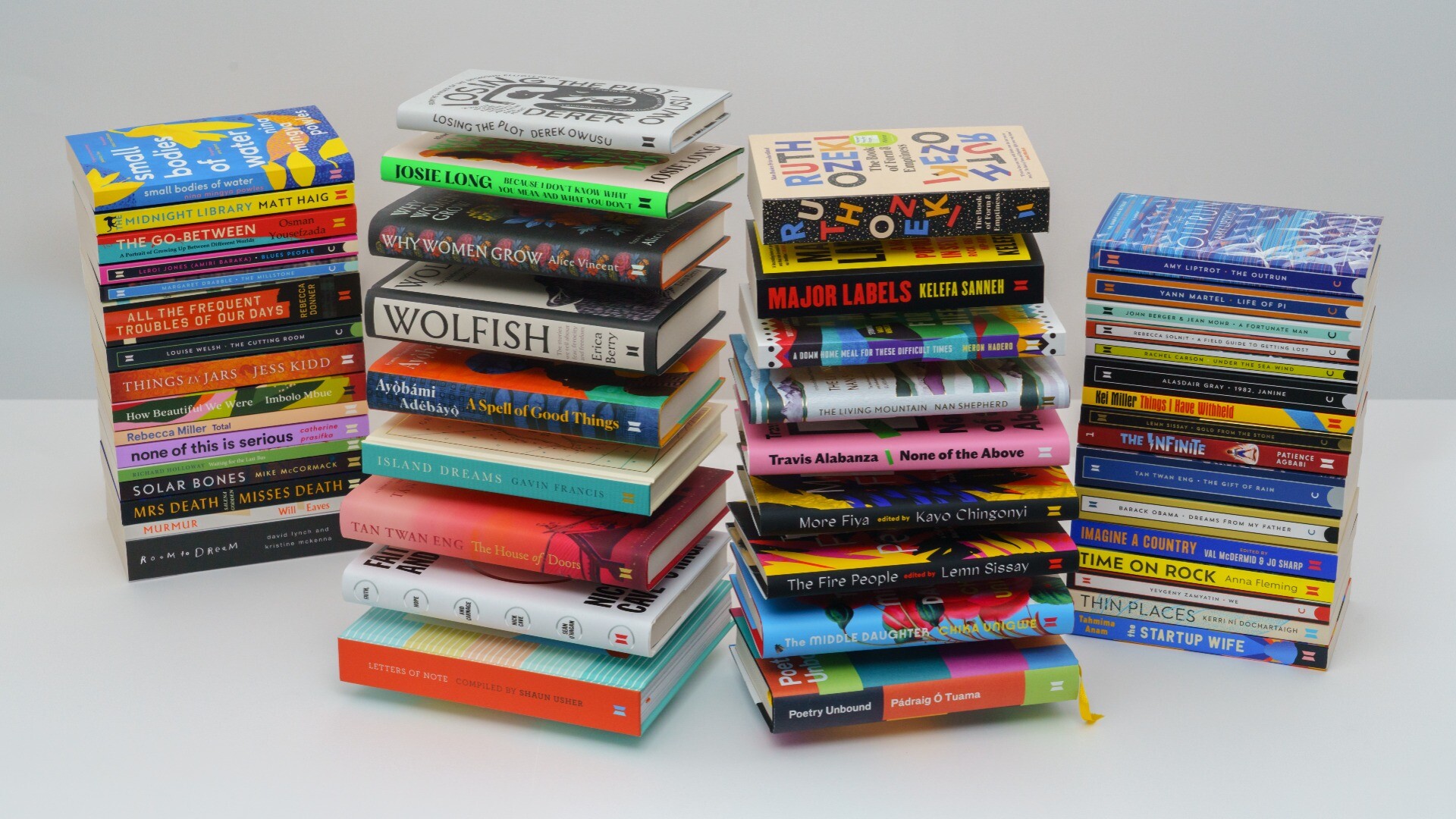 Four big piles of books, photographed on a plain background. There are hardbacks in the central two piles and paperbacks in the outer piles and they all look so dang good.