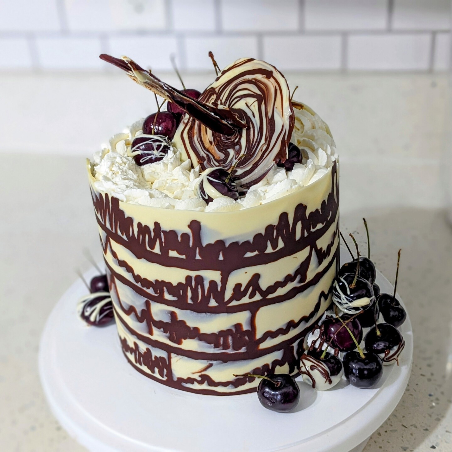 A cake decorated with white and dark chocolate. The chocolate collar has chocolate squiggles that look like quasar spectra. It's topped with cherries and a chocolate disk with a chocolate jet coming out of its center.