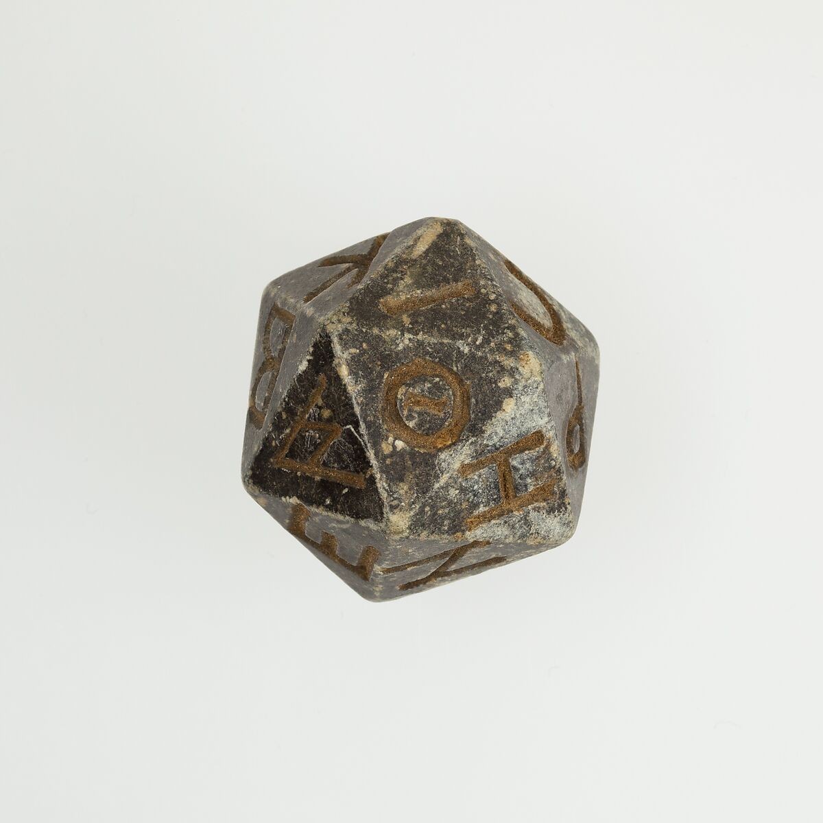 An icosahedron (20 sides) made of rock. It is gray with brown Greek letters carved into each side. It is very worn from use.

Ptolemaic Period–Roman Period
2nd century B.C.–4th century A.D. 

https://www.metmuseum.org/art/collection/search/551072