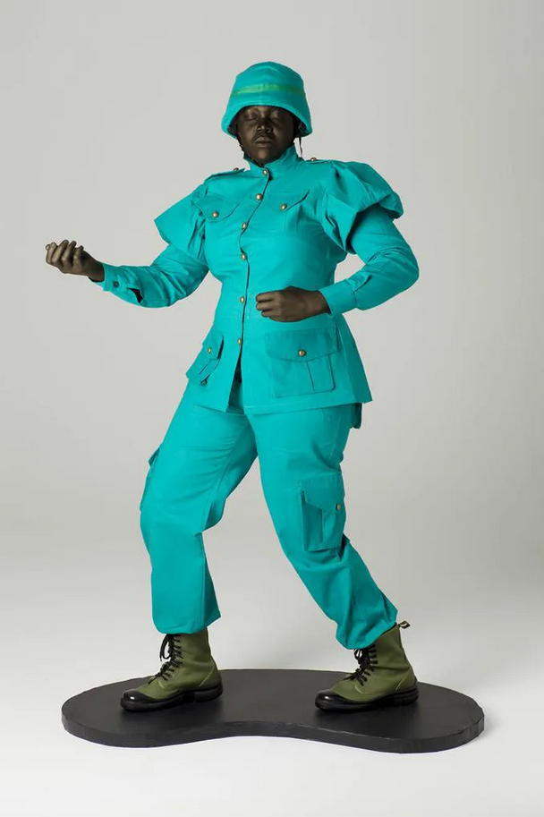 a large sculpture of an african female wearing teal-colored army fatigues, standing with her hands out as if holding a rifle, but there is no rifle, it is like a plastic toy soldier from childhood but in a dream 