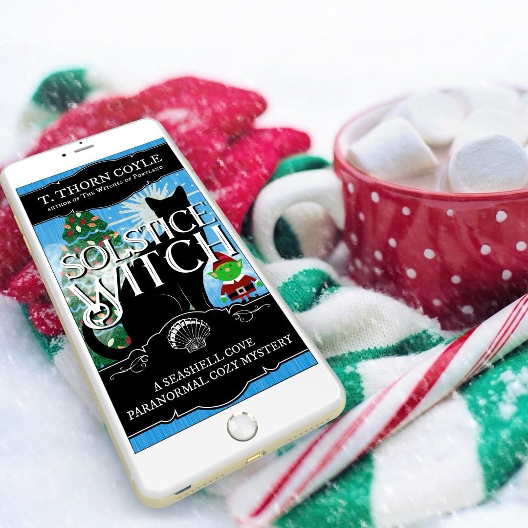 Hot chocolate with marshmallows, a candy cane, mittens, and a phone with Solstice Witch cozy cat mystery.