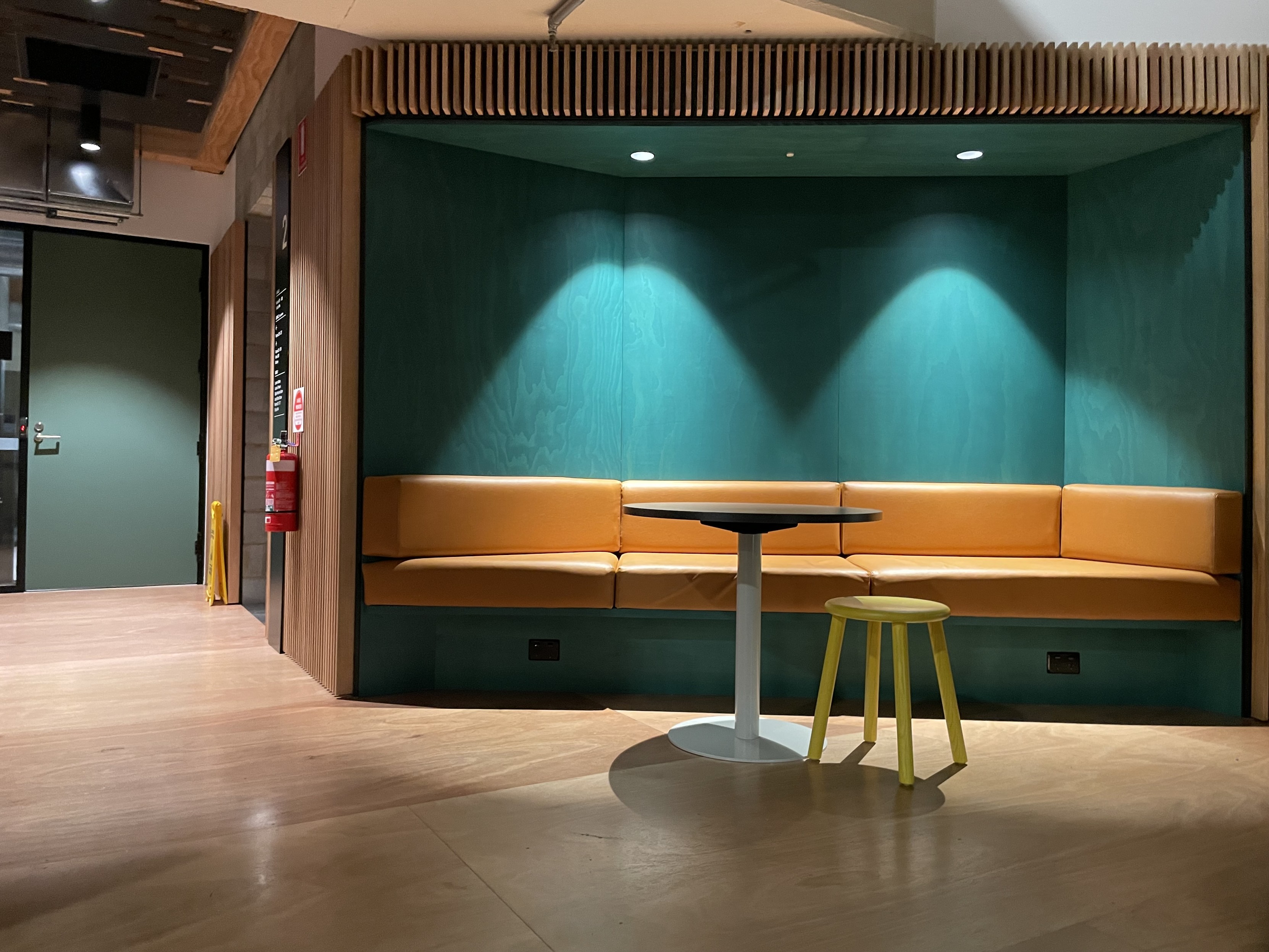 A hall with an alcove where there is a bench seat and a table and stool. Wall painted aqua green. 