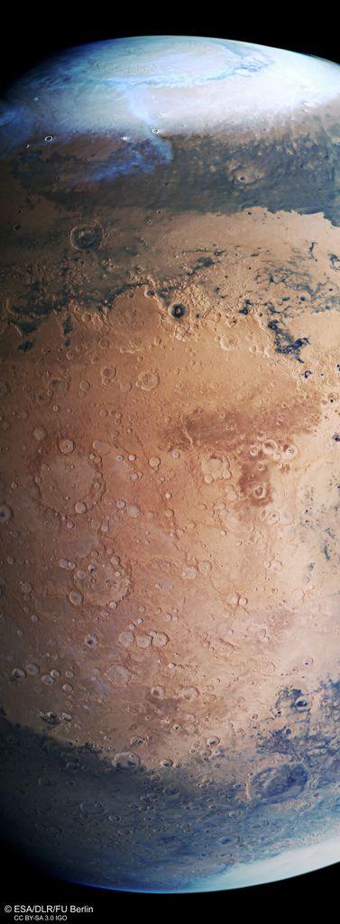 Detailed color photo of the middle third of Mars, from polar cap to polar cap. There are dark swaths of material below the ice caps. In the middle, the planet is covered in orange ground and marked with numerous craters of various sizes.