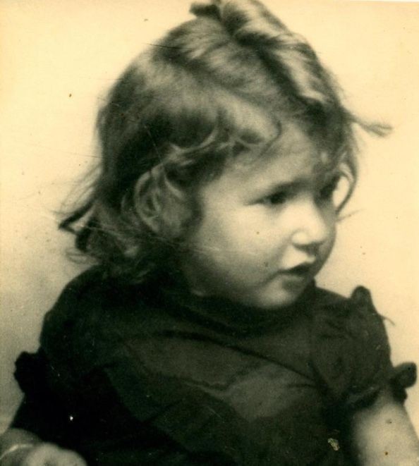 A very young girl with long blond messy hair in a dark short-sleeve blouse.