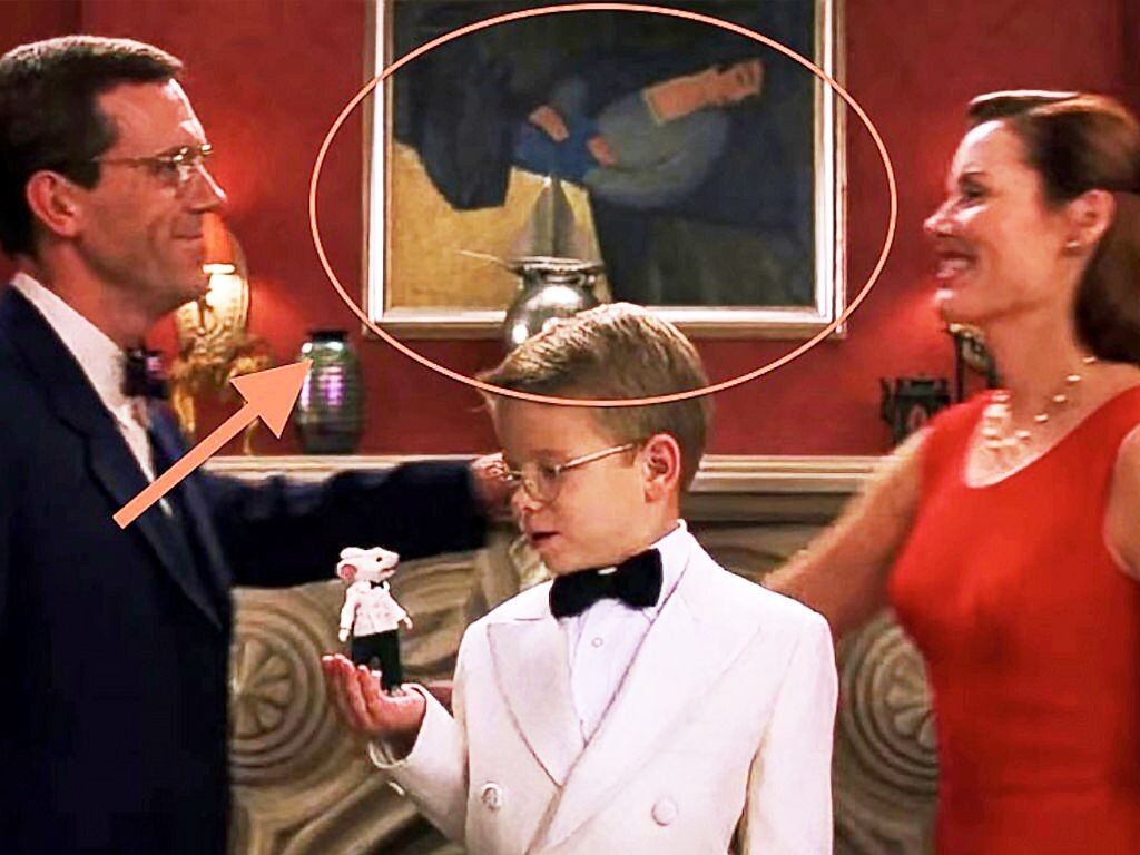 This is a still from the movie "Stuart Little" from 1999.

It shows three people and Stuart. On the very left is Hugh Laurie, wearing a black suit, bowtie, and a crisp white shirt while smiling at Geena Davis to the very right, in her red cocktail dress and white pearls. 

In the middle of the two is Jonathan Lipnicki, aged 9, in a white suit with wide lapels, a white shirt and a black bowtie, looking at his right hand in which he holds animated mouse - dressed in an identical outfit to him - Stuart Little.

Behind them is a fireplace and on the red wall above it, the famous painting.