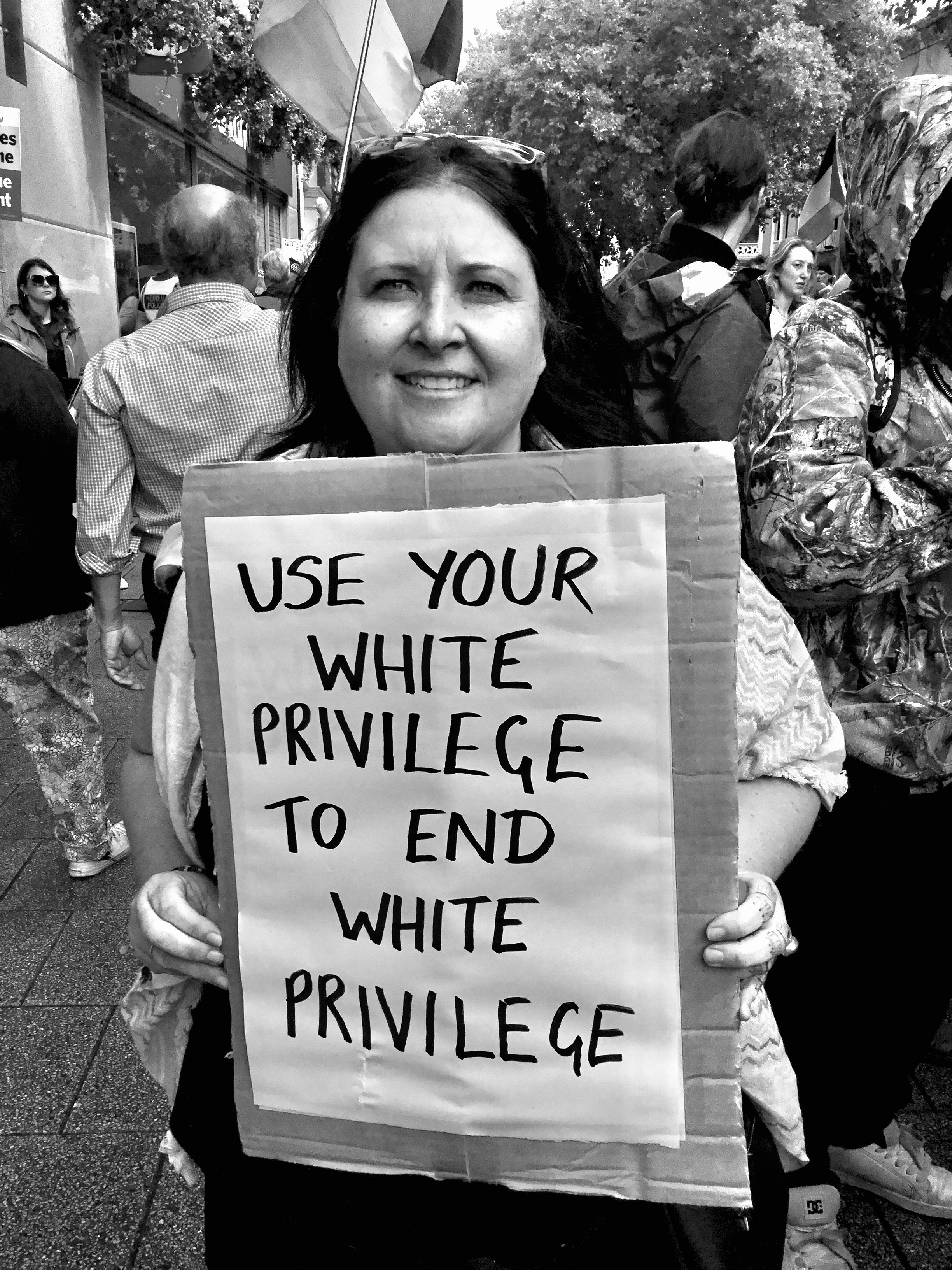 A white person holds a placard that reads “USE YOUR WHITE PRIVILEGE TO END WHITE PRIVILEGE” Black and white image.